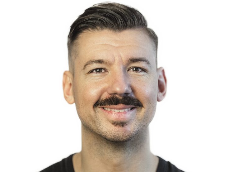 Ein braunhaariger Mann mit Seitenscheitel und Schnauzbart.