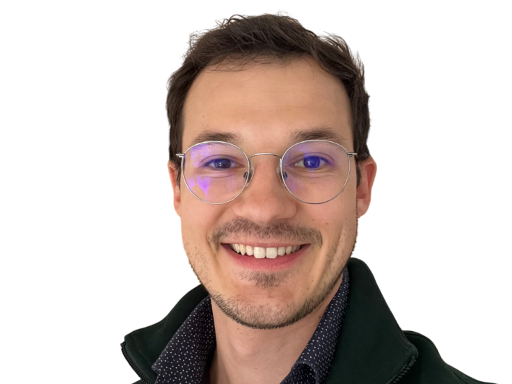 Ein Mann mit dunklen, kurzen Haaren und Brille mit dünnem, silbernen Brillengestell lächelt in die Kamera. Er trägt ein dunkelblaues gepunktetes Hemd und darüber einen schwarzen Fleece-Pullover.