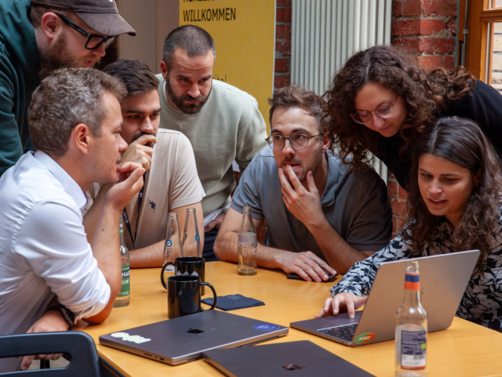Eine Gruppe von Menschen sitzt um einen Tisch und arbeitet konzentriert gemeinsam an einem Laptop